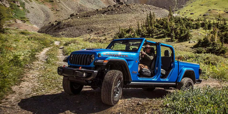 Blue 2026 Jeep Gladiator driving off-road on a mountain trail