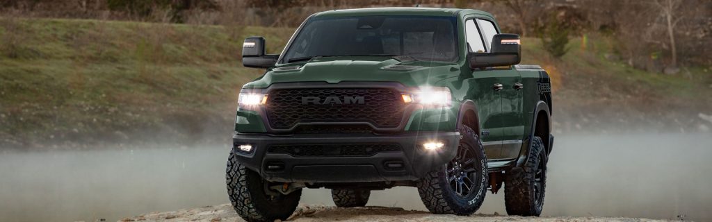 Green Ram 1500 Rebel pickup truck parked beside a misty lake, showcasing its rugged off-road capability and bold design.