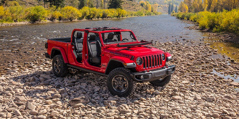 rigt angle of a red 2024 jeep gladiator parked on rocks by river