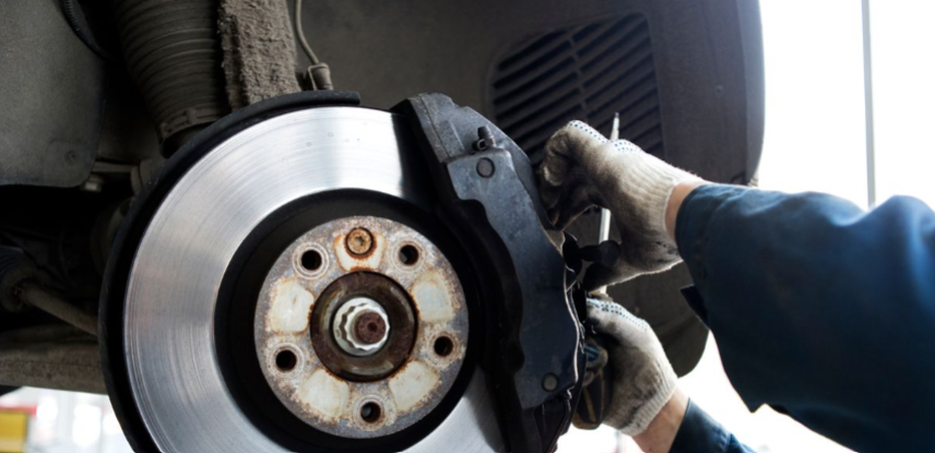 Mechanic inspecting a vehicle brake rotor and caliper during a brake service repair.